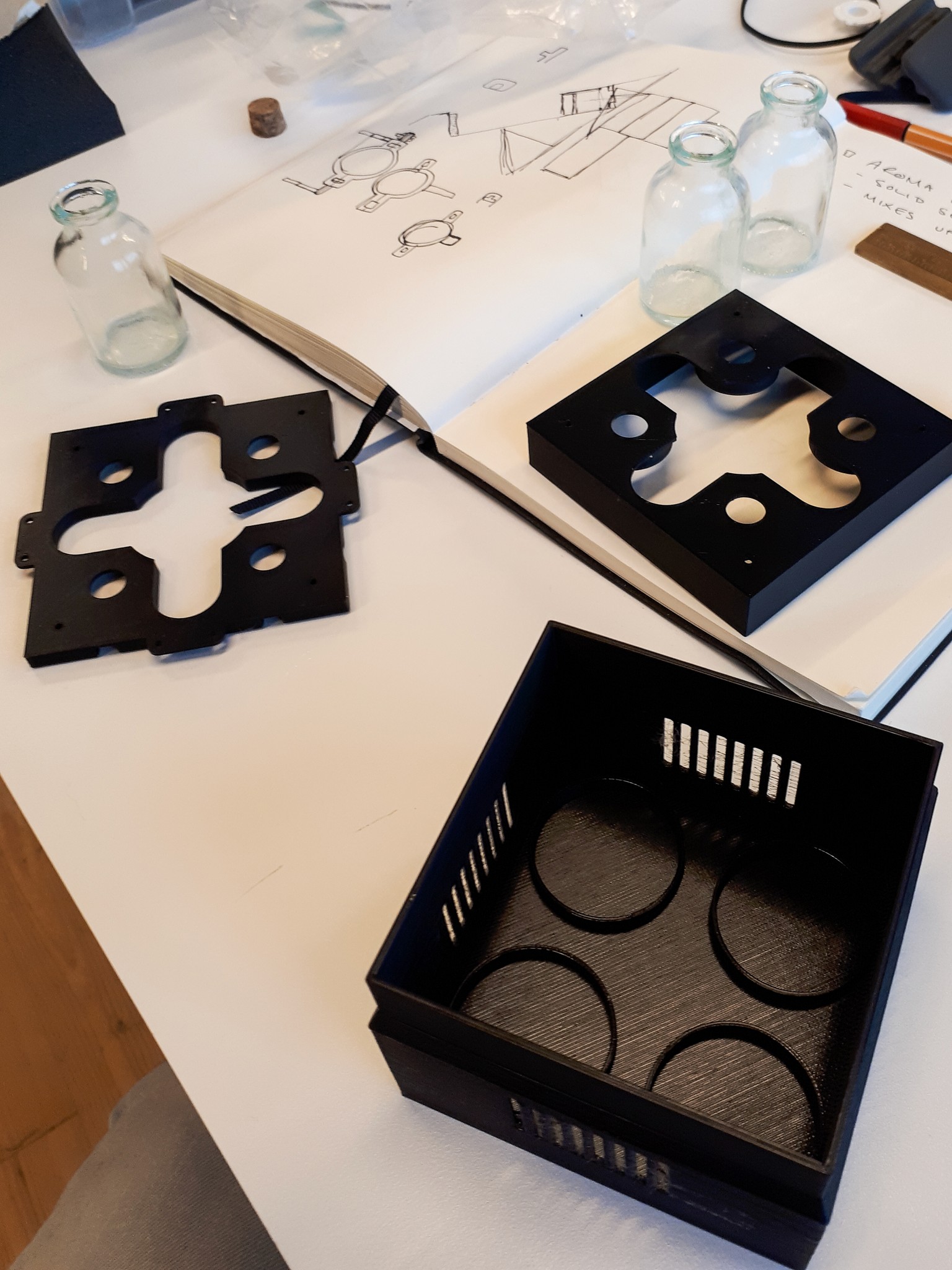 a black 3d printed box with 4 round spots on it for fragrance bottles and groves on the sides for ventelation