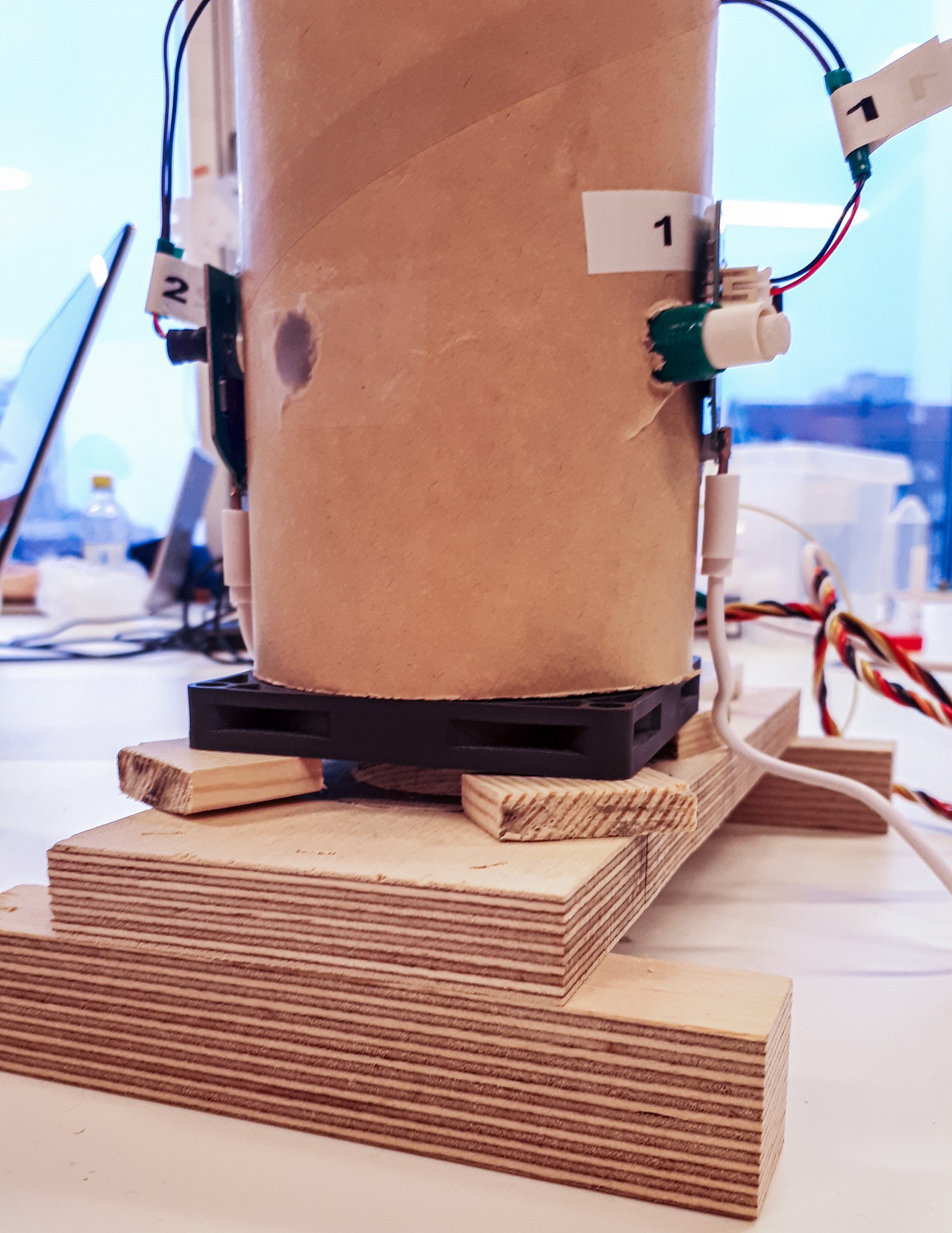 a side picture of a wooden base with fan mounted to it at the bottom and the fanning system of scentony device mounted on the top with wires hanging to the side