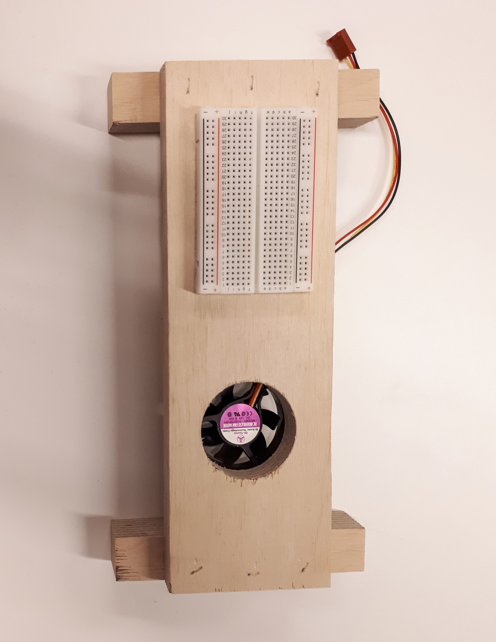 a wooden base with a fan mounted to it and a breadboard on the side