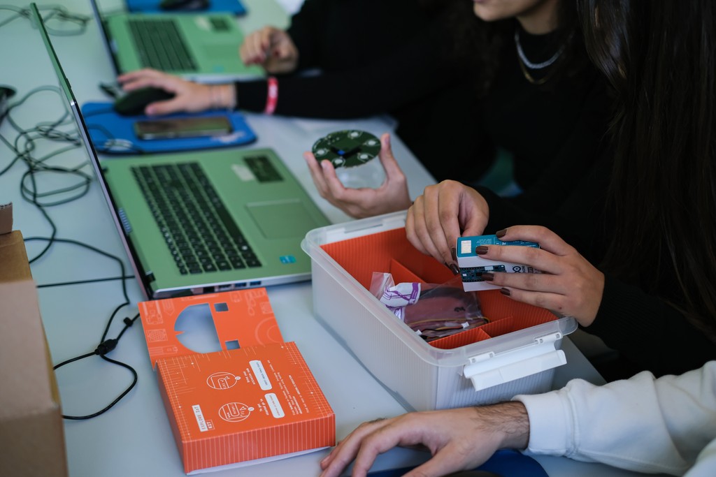 Close-up of multiple hands using the Arduino Explore IoT Kit and keyboards on a desk during usability testing session
